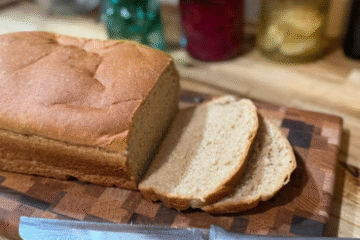 a loaf of bread with some pieces sliced on a wooden cutting board