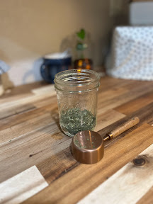 pint jar on a wooden counter filled part of the way with dried herbs and a copper measuring cup in front