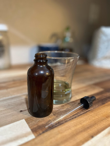 dropper bottle sitting on a wooden counter with a glass in the background with a little bit of water
